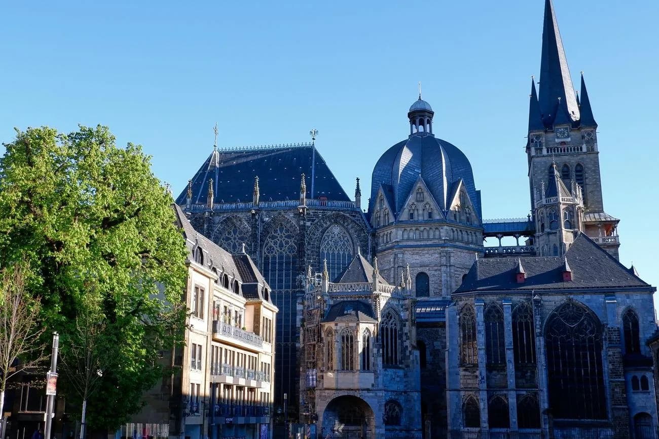 Extérieur de la cathédrale d'Aix-la-Chapelle : octogone carolingien à dôme, chœur gothique et clocher, sous un ciel bleu