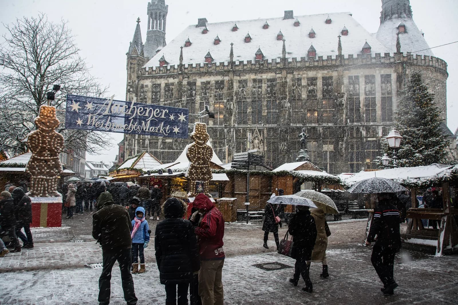 Marché de Noël d'Aix-la-Chapelle sous la neige, avec ses chalets et l'hôtel de ville en arrière-plan