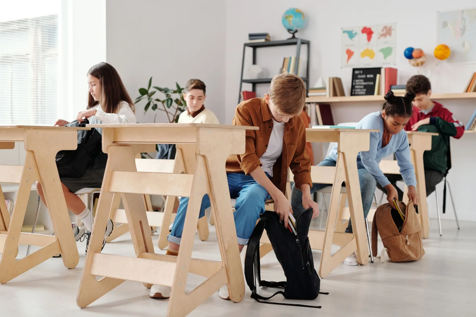 Élèves assis à des bureaux en bois dans une salle de classe, l'un sortant ses affaires de son cartable