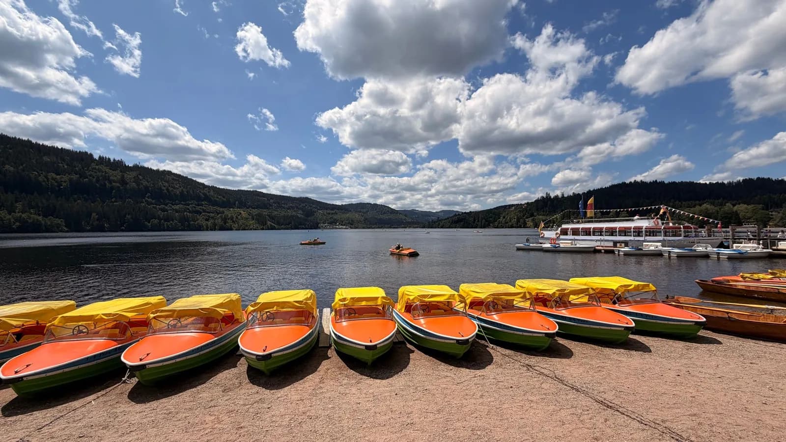Pédalos colorés amarrés sur la rive du lac Titisee, avec les collines boisées de la Forêt-Noire en arrière-plan