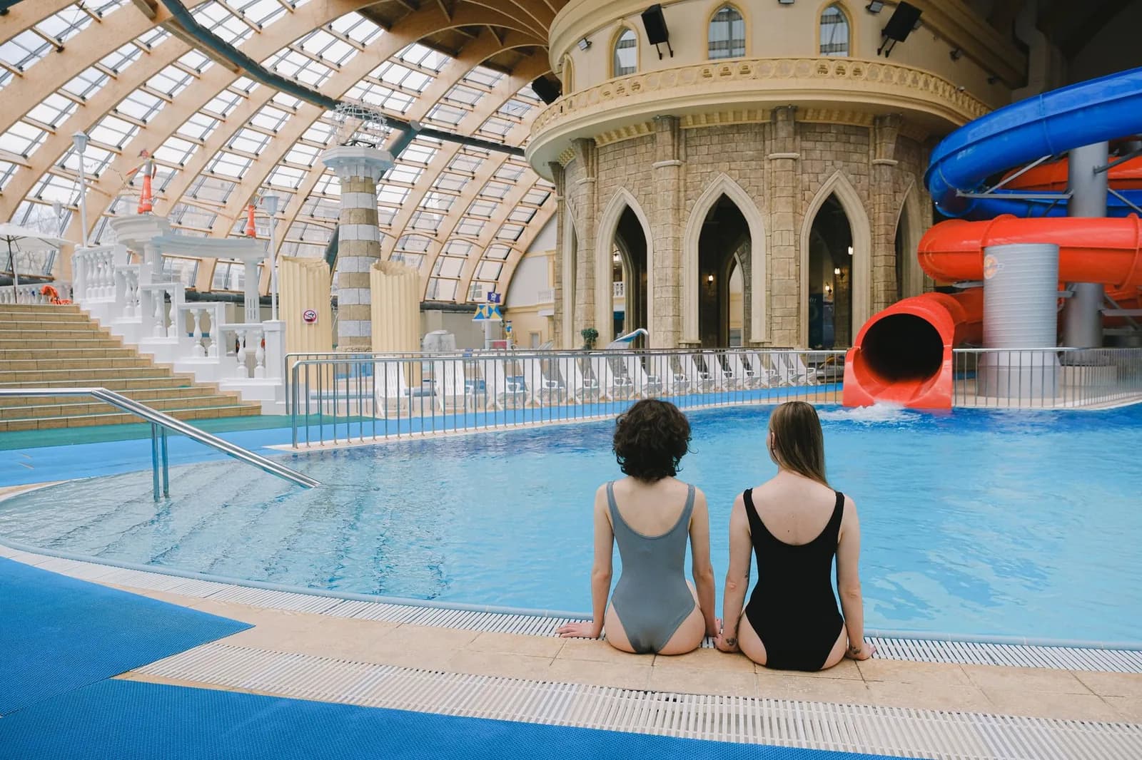 Halle de parc aquatique couvert sous une verrière, avec bassin intérieur et toboggans rouge et bleu