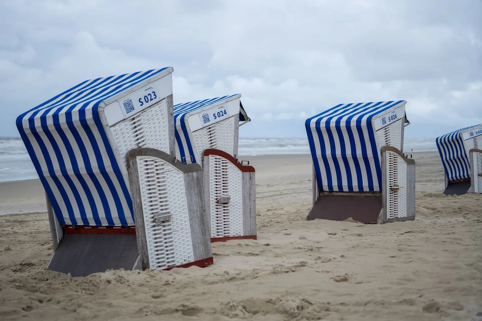 Strandkörbe à rayures bleues et blanches alignés sur une plage de la mer du Nord, sous un ciel nuageux